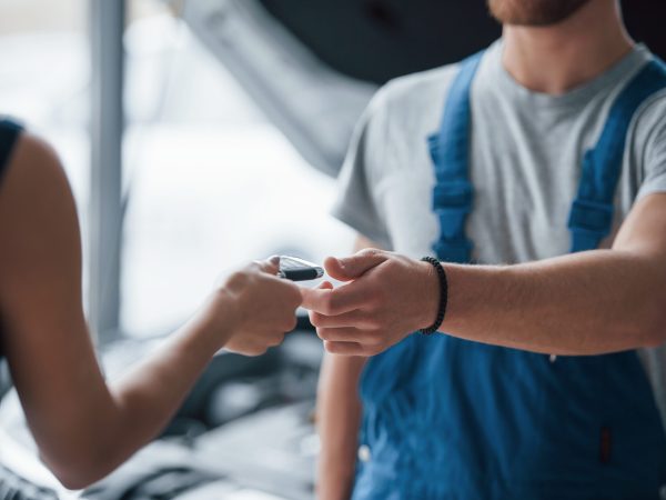Process of giving the keys. Woman in the auto salon with employee in blue uniform taking her repaired car back.